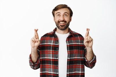 Mann schaut nach oben und kreuzt Zeigefinger und Mittelfinger